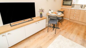 Une cuisine moderne équipée d’un téléviseur à écran plat, de meubles en bois, d’une table à manger avec des chaises et d’un petit îlot central avec une machine à café.