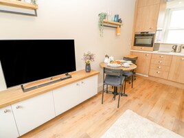 A modern kitchen with a flat-screen TV, wooden cabinets, a dining table with chairs, and a small island with a coffee machine.