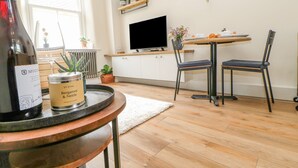 Une cuisine moderne avec un plancher en bois, une table à manger avec des chaises, un téléviseur et une bouteille de vin posée sur un plateau.