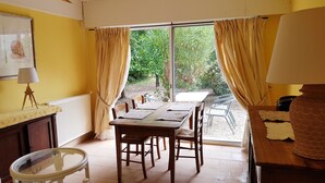 A dining area with a table and chairs, a lamp, and a view of greenery outside. - Alpilles Cottage Philippe's Farm pool shared (Saint-Rémy-de-Provence)