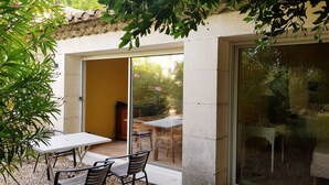 An outdoor patio with a table and chairs, a stone wall, and a sliding glass door leading to an outdoor area. - Alpilles Cottage Philippe's Farm pool shared (Saint-Rémy-de-Provence)