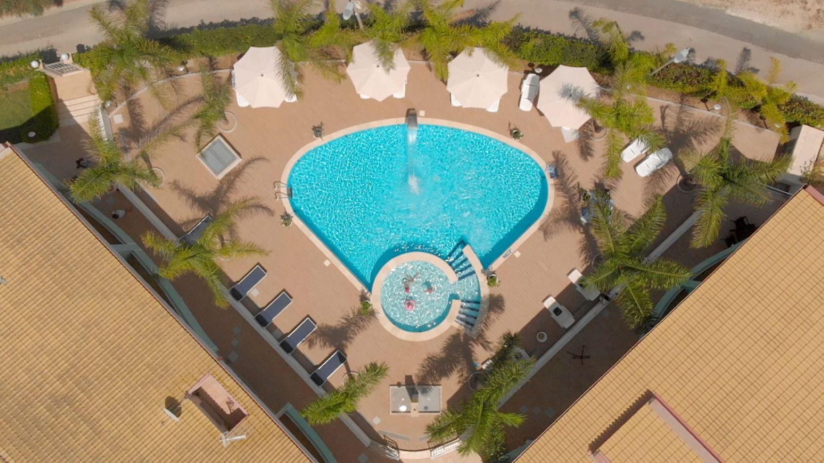 An aerial view of a swimming pool surrounded by palm trees and sun loungers.
