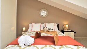 Ein ordentlich gemachtes Bett mit roter Decke, ein Nachttisch mit Lampe und ein an der Wand befestigter Spiegel.