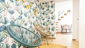 Une pièce comprenant deux fauteuils en osier, un tapis tissé et un mur orné d’un motif de feuilles tropicales.