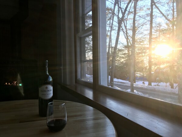 A bottle of Clos du Bois wine and a glass on a wooden table by a window with a view of trees and a snowy landscape.