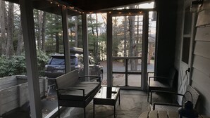 A covered porch with a stone floor, two wicker chairs, a small table, and a lantern. - Cozy Lakeview Family Cottage - steps to the lake, 2 swim docks & restaurant! (Hawley)