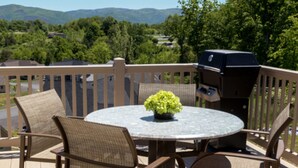 Ein runder Tisch mit Korbstühlen, einem Grill und einem Blumentopf auf einem Balkon mit Blick auf Berge und Häuser.