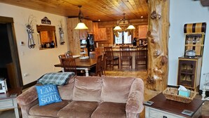 A cozy cabin interior with a brown sofa, wooden dining table, and a kitchen area.