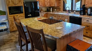 A kitchen with wooden cabinets, a granite countertop, a black refrigerator, and a sink.
