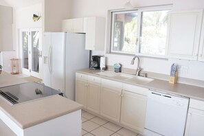 Una cucina moderna con mobili bianchi, piano cottura nero, macchina per caffè e lavastoviglie.