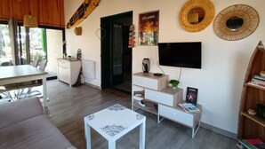 Un salon moderne comprenant un coin repas, des poutres apparentes en bois au plafond, un téléviseur à écran plat, des miroirs décoratifs et une bibliothèque.