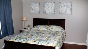 Un dormitorio con una cama de madera, una mesita de noche pequeña con una lámpara, y tres obras de arte florales colgadas en la pared.
