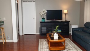 Una sala de estar con televisión de pantalla plana, un sofá, una mesa de centro y una lámpara.