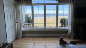 A bedroom with a large arched window, wooden flooring, a bed, a TV, and a suitcase. - Executive Water View Home With Hot Tub, Just 3 Minutes To Barachois Beach (South Rustico)