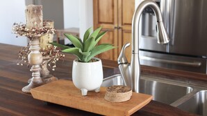 A wooden serving board with a potted plant, a candle, and coasters on a kitchen counter. - Executive Water View Home With Hot Tub, Just 3 Minutes To Barachois Beach (South Rustico)