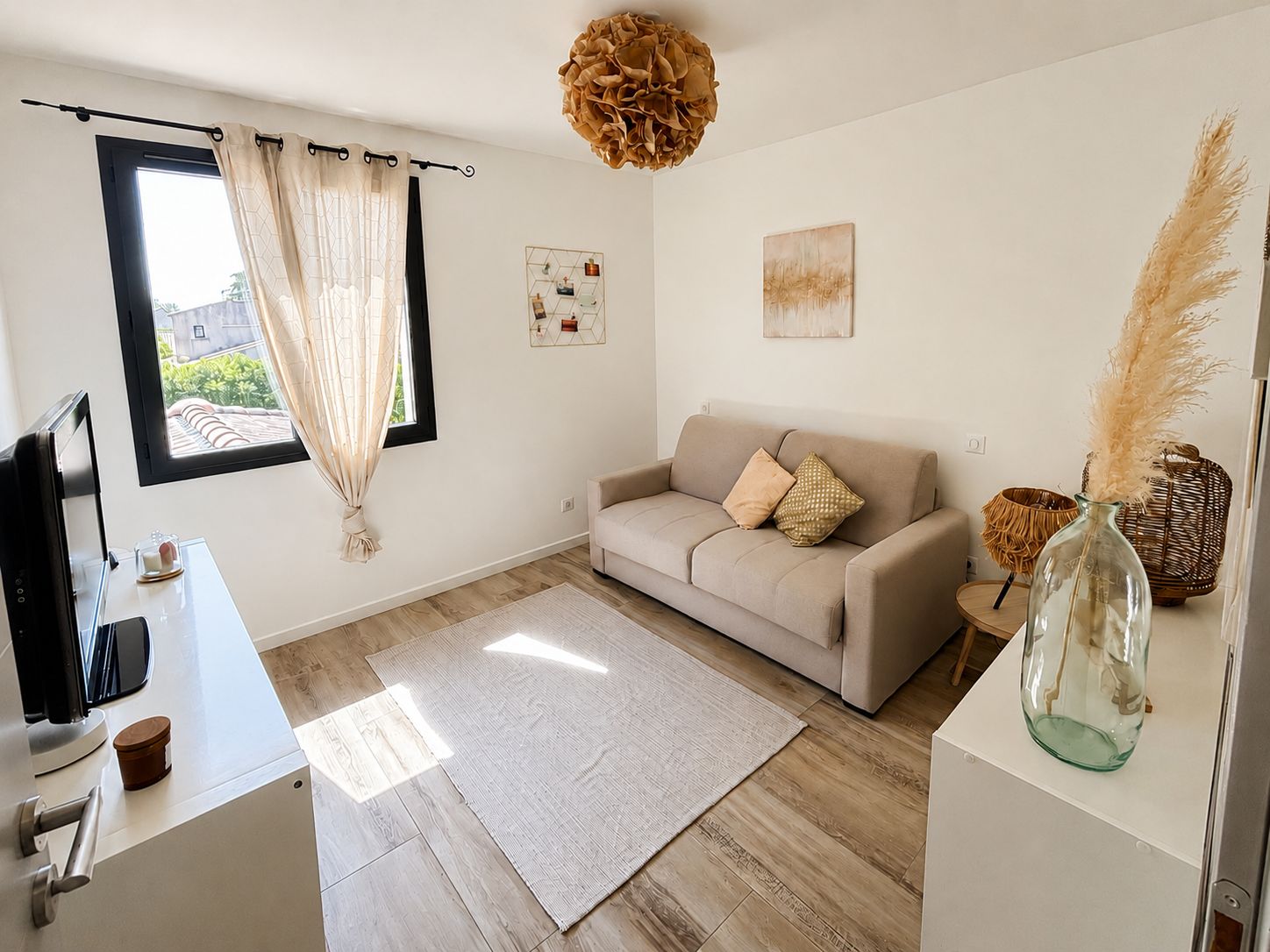 A modern living room with a sofa, a coffee table, a TV, and a large window with curtains.