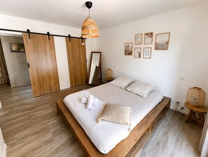 A bedroom with a large bed, wooden floor, a hanging light fixture, and a sliding door.