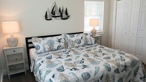 Ein Schlafzimmer mit Bett, Nachttischen, einer Lampe, Wanddeko, einem Fenster mit Jalousien und einem Kleiderschrank.