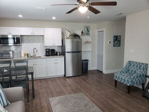 A modern kitchen with a microwave, toaster, and coffee maker, a dining area with chairs, and a patterned armchair. - "Barefoot Bungalow",1br/1ba for familes up to 3 (Panama City Beach)