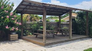 Ein überdachter Patio-Bereich mit Picknicktischen, einer Holzterrasse und einem blühenden Baum.