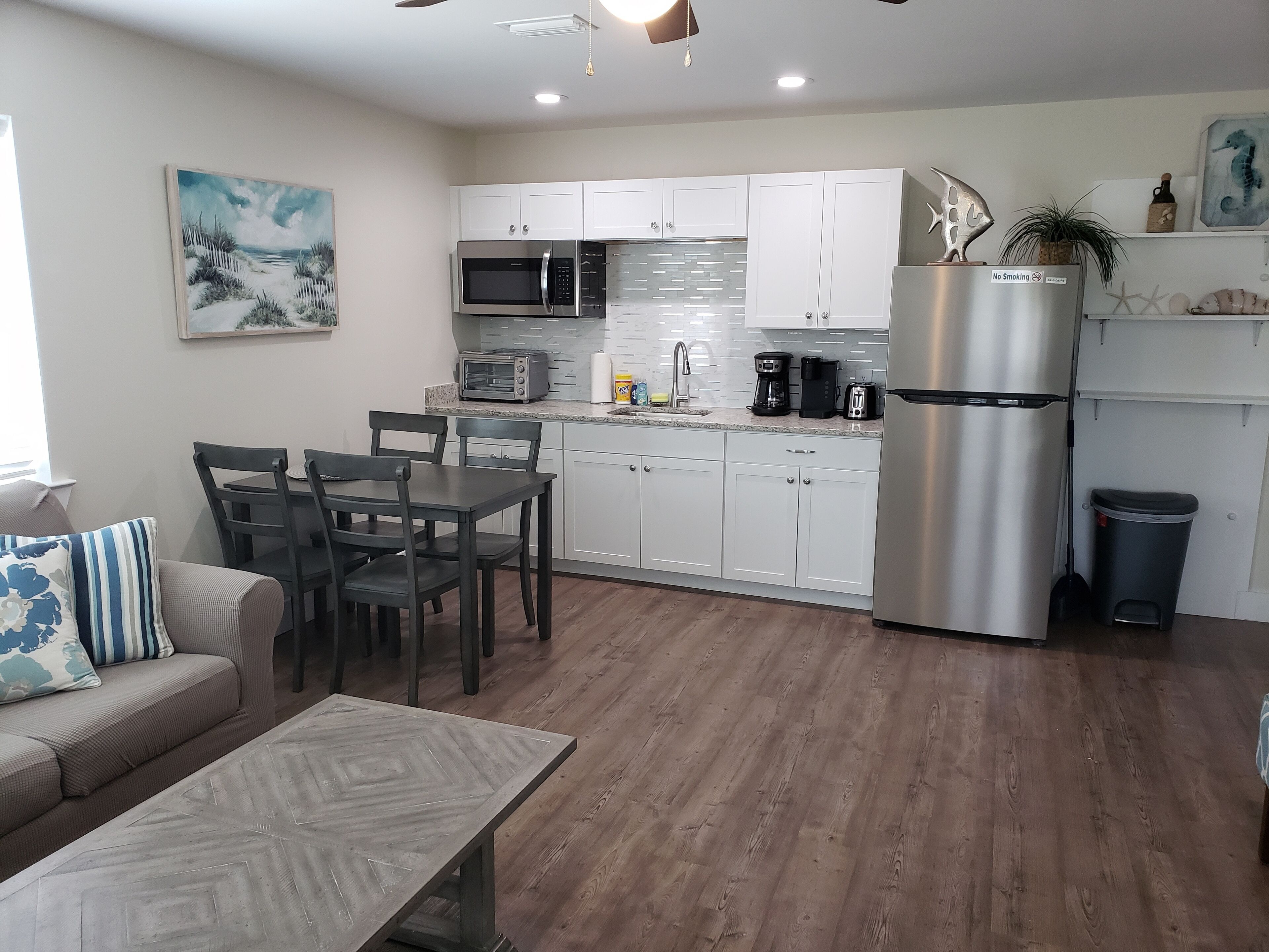 Una cocina moderna con gabinetes blancos, electrodomésticos de acero inoxidable y una zona de comedor con mesa y sillas de madera.