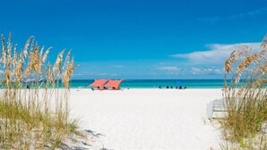 Een strand met wit zand, een rode strandparasol en hoge grassen.