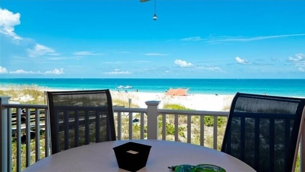 Een tafel met een zwart voorwerp, met uitzicht op een strand met helderblauw water en een zandstrand.