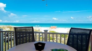 A table with a black object on it, overlooking a beach with clear blue water and a sandy shore. - Anna Maria Island Club 11, Condo 2 Bedroom/ 2 Bath Gulf view, maximum occupancy of 4 people. Community pool, Max 1 vehicle. (Bradenton Beach)
