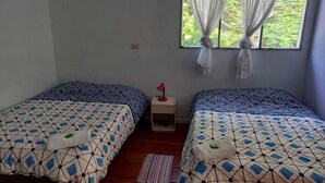 Una habitación con dos camas, cada una con ropa de cama estampada, una mesita de noche pequeña con una lámpara y una ventana con cortinas de tul.