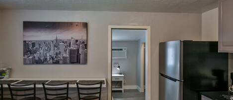 A modern kitchen with a black refrigerator, a dining area with four bar stools, and a cityscape painting on the wall.