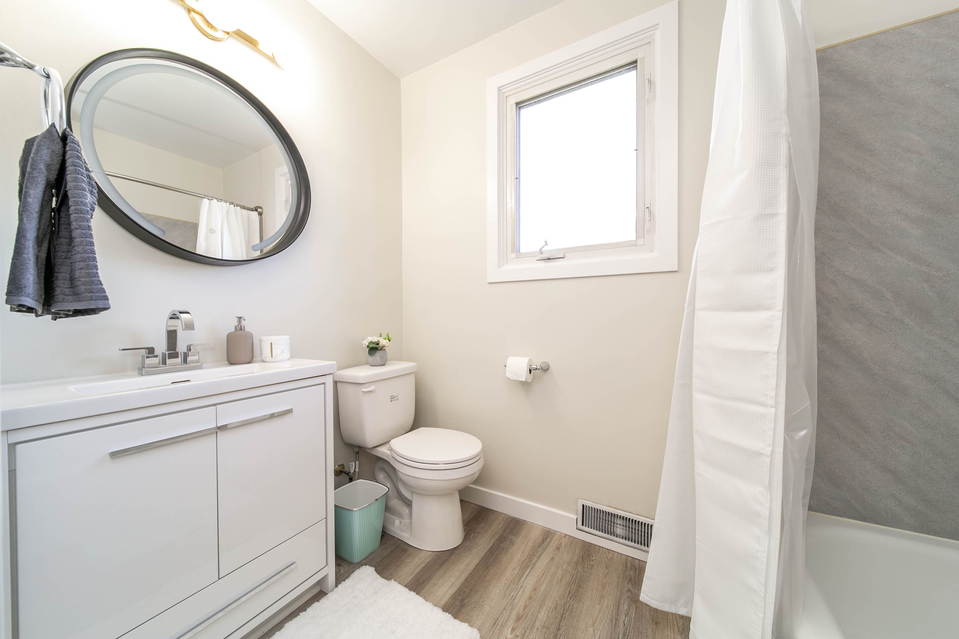 Une salle de bain avec un meuble-lavabo blanc, un miroir rond, des toilettes et un rideau de douche.