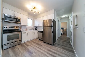 Una cocina moderna con electrodomésticos de acero inoxidable, armarios blancos y piso de madera.