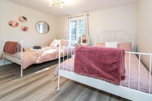 Un dormitorio con dos camas, una ventana con cortinas, un espejo y una mesita de noche con lámpara.