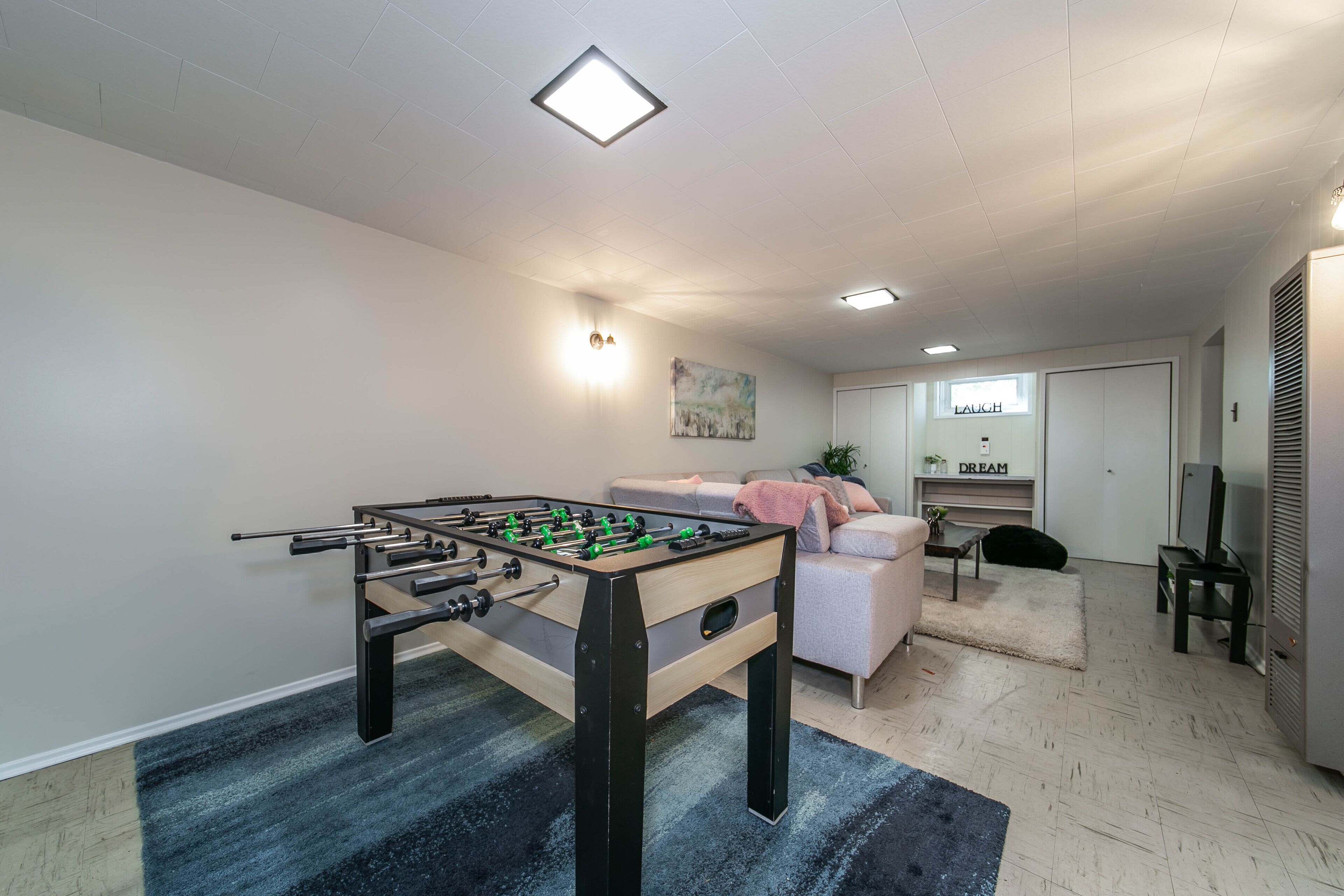 Een kamer met een tafelvoetbaltafel, een bank, een televisie en een kast.