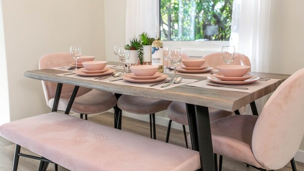 A dining table set with pink bowls, plates, and wine glasses, surrounded by matching chairs. - ★6B Modern Bungalow★King Bed/WiFi✔Long Stays★Clean (Edmonton)