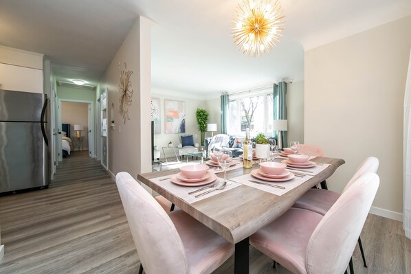 Una cocina moderna con refrigerador de acero inoxidable, piso de madera y una zona de comedor con sillas rosadas y una mesa de madera dispuesta para cuatro.