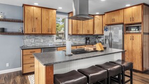 Una cocina moderna con armarios de madera, un refrigerador de acero inoxidable, una isla integrada con taburetes y un ventanal grande.