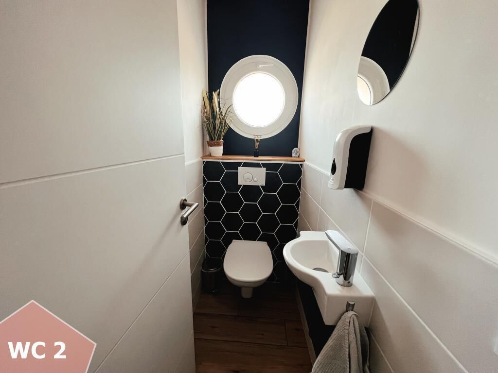 A compact WC with a round mirror, a small sink, and a potted plant.
