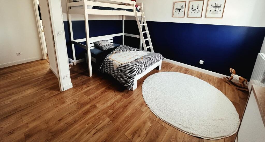 Une chambre avec des lits superposés, un plancher en bois, un tapis rond et des tableaux encadrés accrochés au mur.