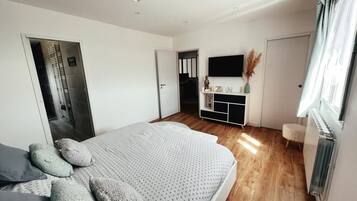 A modern bedroom with a large bed, a TV mounted on the wall, and a radiator.