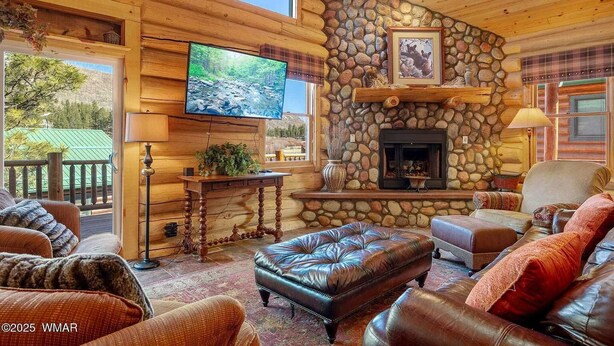 A cozy log cabin interior with a stone fireplace, leather furniture, and a large TV on the wall. - Greer Riverside Getaway (Cabin 168) (Greer)