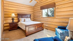 A log cabin bedroom with a wooden bed, a nightstand with a lamp, a window, and a ceiling fan. - Greer Riverside Getaway (Cabin 168) (Greer)