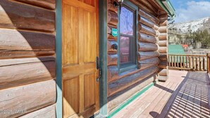 A log cabin with a wooden door and a window, a porch with a railing, and a view of a snowy mountain. - Greer Riverside Getaway (Cabin 168) (Greer)