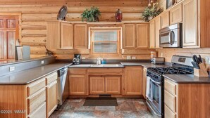 A kitchen with wooden cabinets, a microwave, a stove, and a coffee maker. - Greer Riverside Getaway (Cabin 168) (Greer)