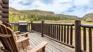 En träaltan med Adirondack-stolar och en grill, med utsikt över ett bergigt landskap.