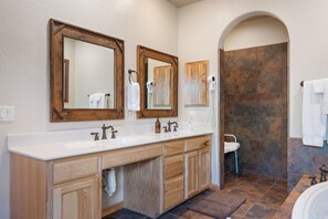 A bathroom with a wooden vanity, double sinks, and a shower area. - Greer Cowboy Lodge (Cabin 169) (Greer)