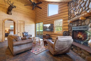 Cozy cabin interior with a stone fireplace, leather sofa, and a large mirror.