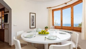 A round dining table with white chairs, a plate of green apples, and a pitcher of water.