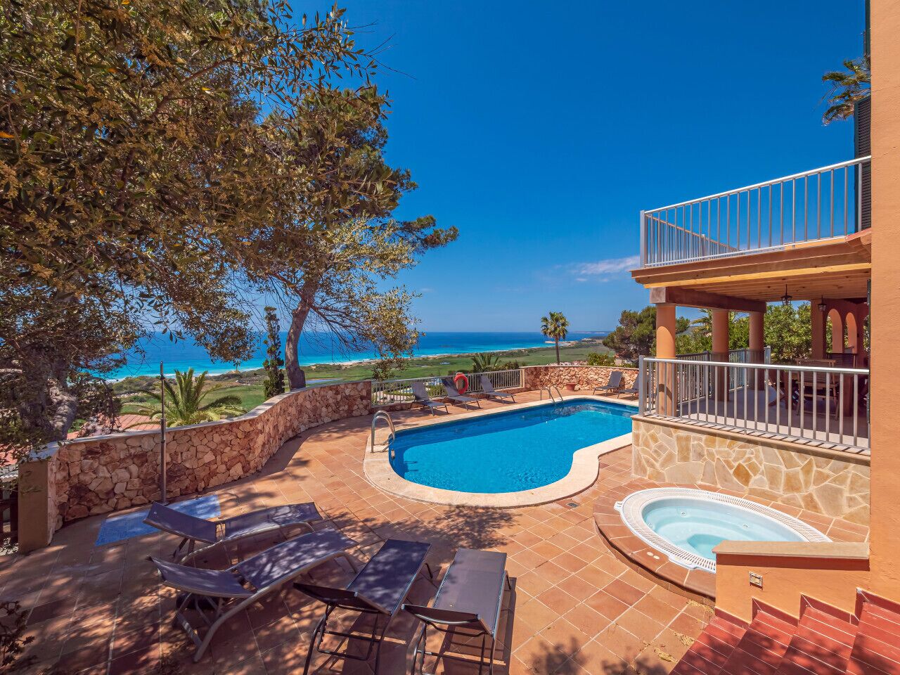 A pool area with a view of the ocean, stone walls, and lounge chairs.