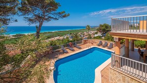 A pool with a view of the ocean, surrounded by lounge chairs and a stone wall.
